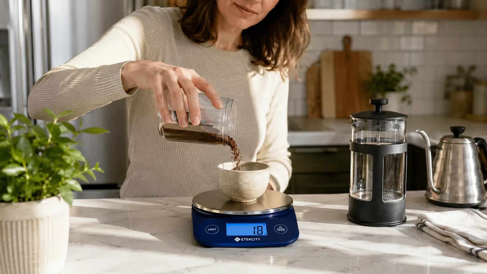 A hand weighing coffee grounds on a digital kitchen scale before brewing a pot of coffee