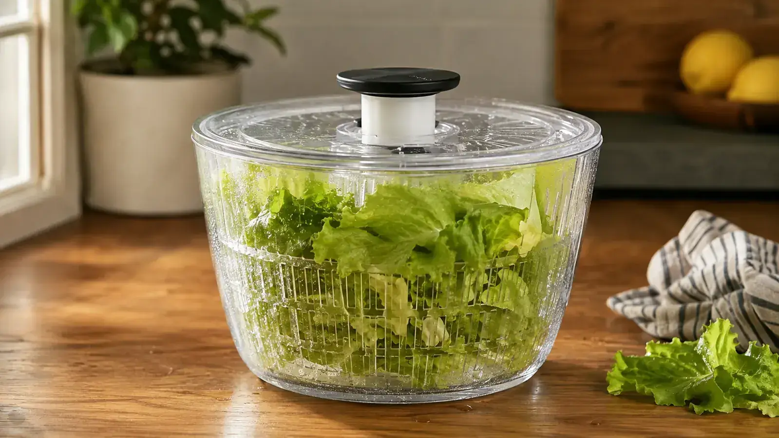 Glass salad spinner filled with freshly washed lettuce leaves on a kitchen counter in soft morning light