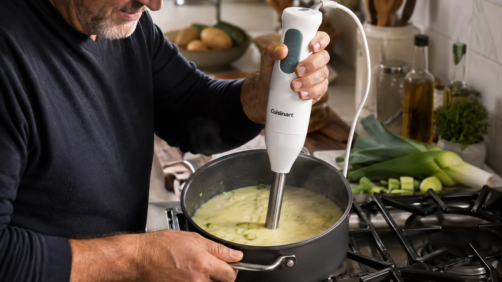 Hand holding an immersion blender fully submerged in a pot of soup, blending directly in the pot