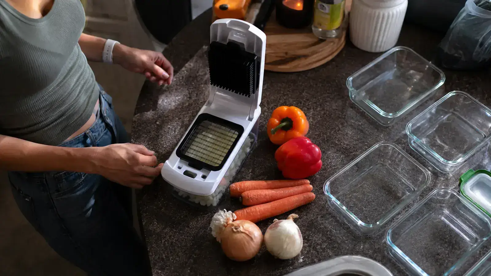 A home kitchen counter set up for Sunday meal prep with a white vegetable chopper, cutting board, and rows of glass containers ready to be filled