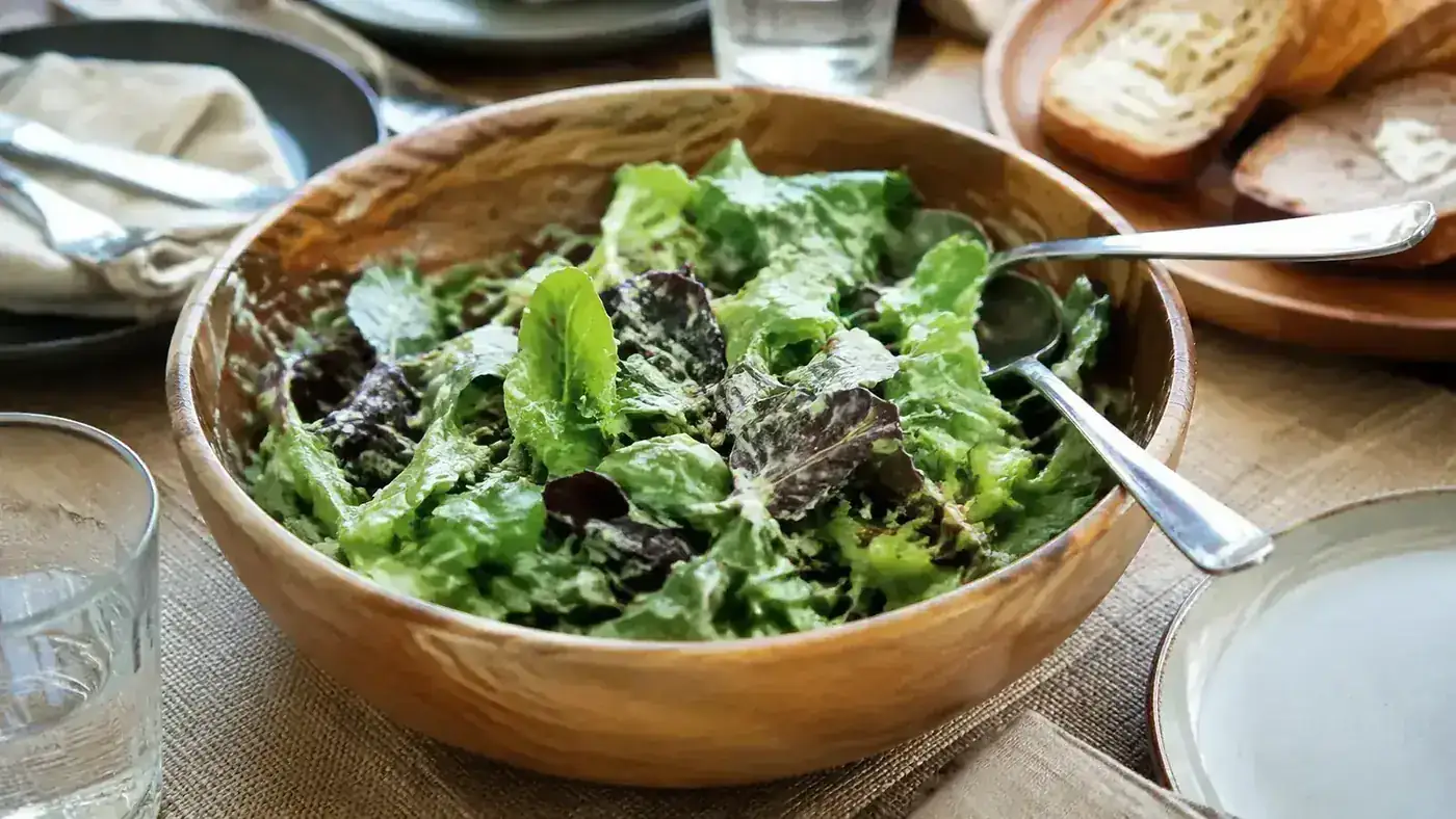 A dressed green salad with dressing clinging evenly to dry lettuce leaves on a kitchen table